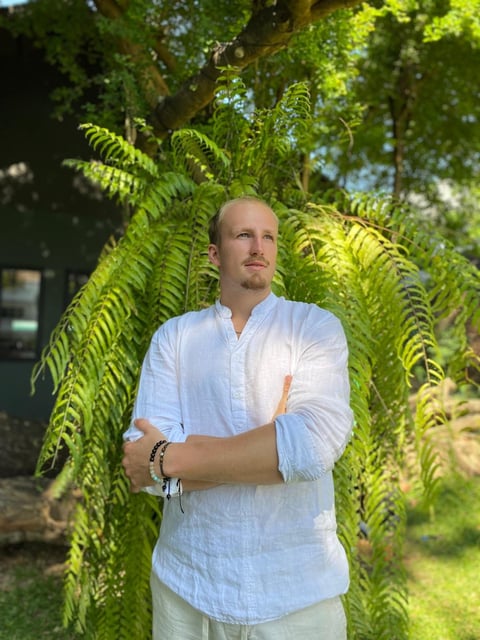 Man in light blue shirt standing under hanging fern vines in sunlit garden setting